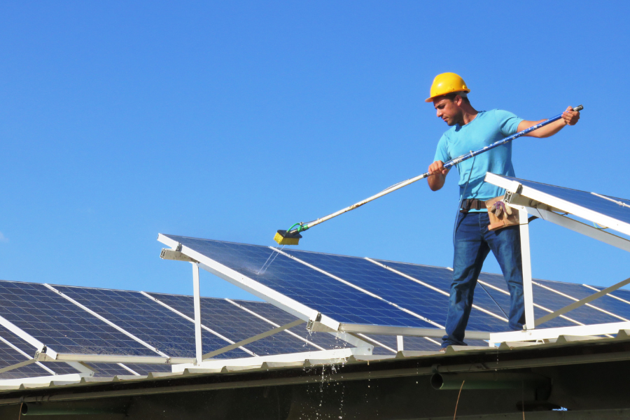 Workman cleaning solar panels with brush and water