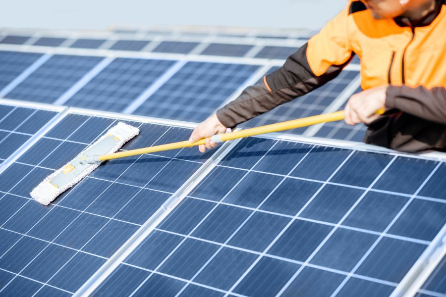 Workman cleaning solar panels with a mob