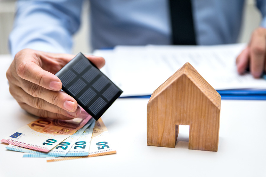 Banker holding solar panel with Euros and wooden house